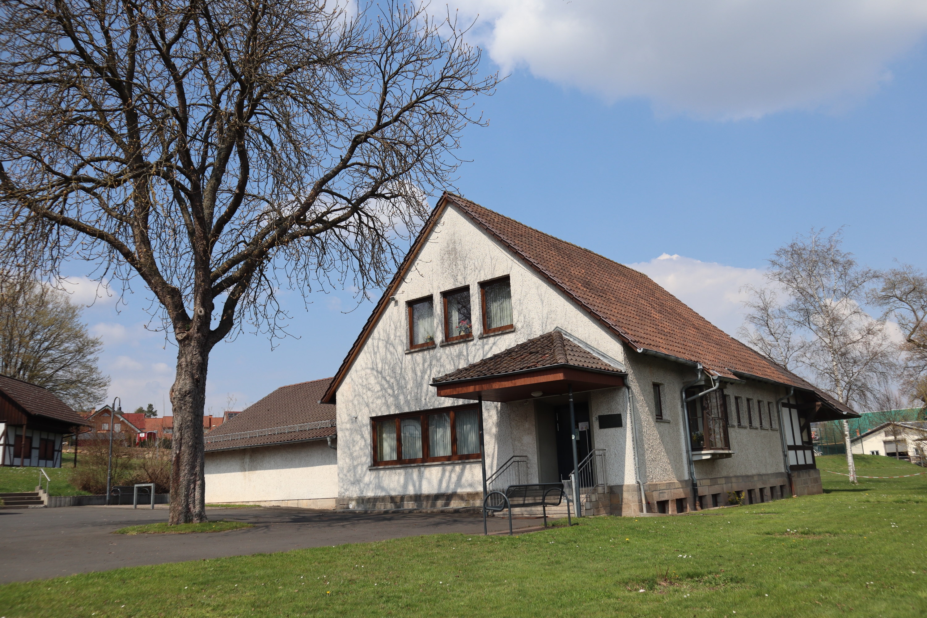 Freistehendes, weißes Haus - Dorfgemeinschaftshaus, umgeben von grüner Wiese und einem Baum.