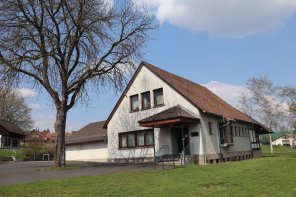 Freistehendes, weißes Haus - Dorfgemeinschaftshaus, umgeben von grüner Wiese und einem Baum.