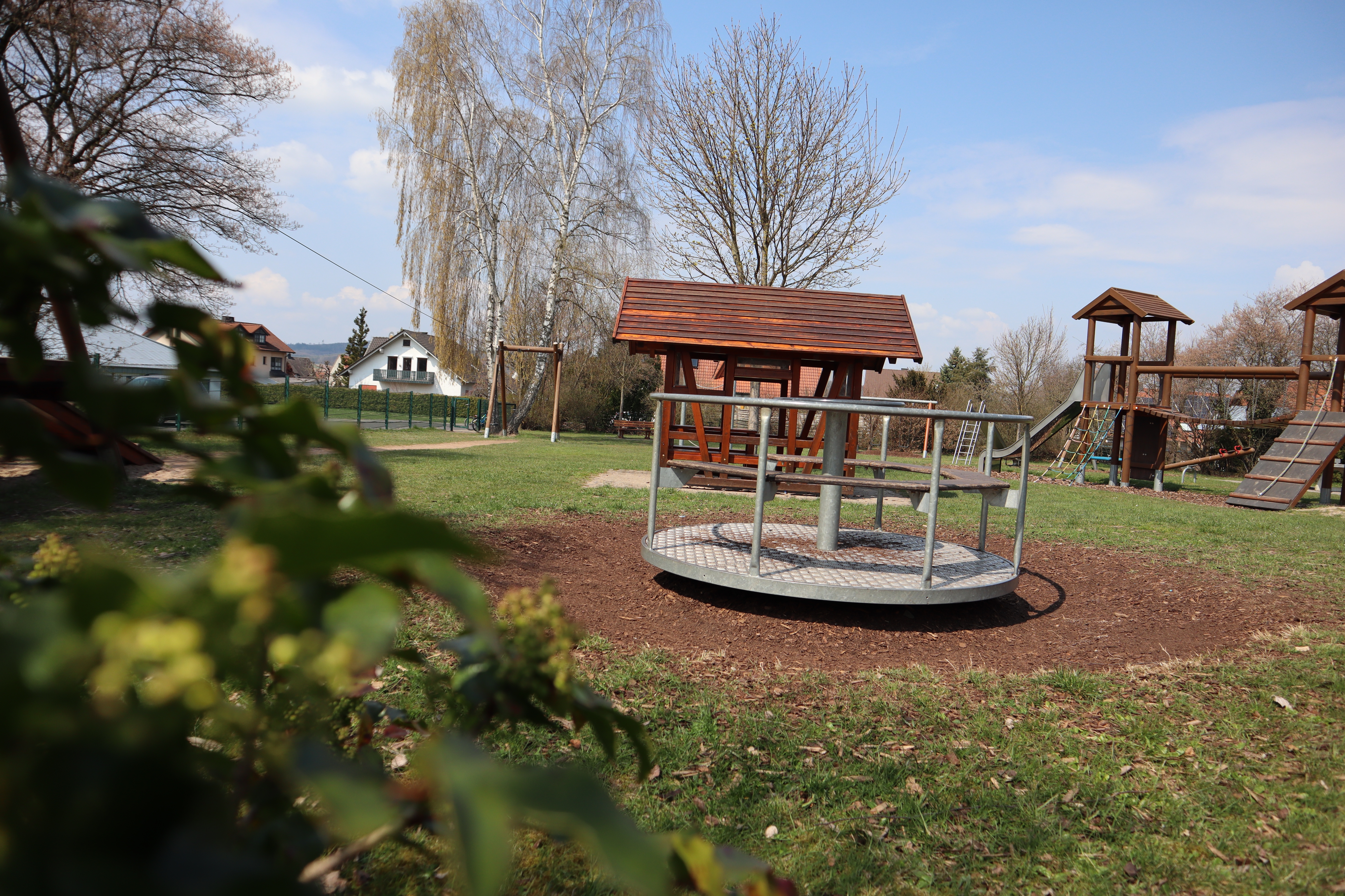 Spielplatz_St.Damian.Str. Spielplatzgeräte, welche hinter einem Busch fotografiert wurden. U.a. Karussell