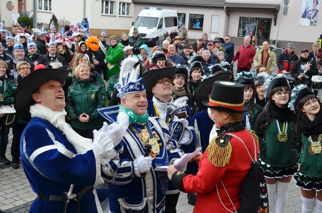 Ein Prinz auf dem Rathausvorplatz, der in ein Mikrofon spricht. Dahinter stehen Karnevalisten versammelt und hören zu.