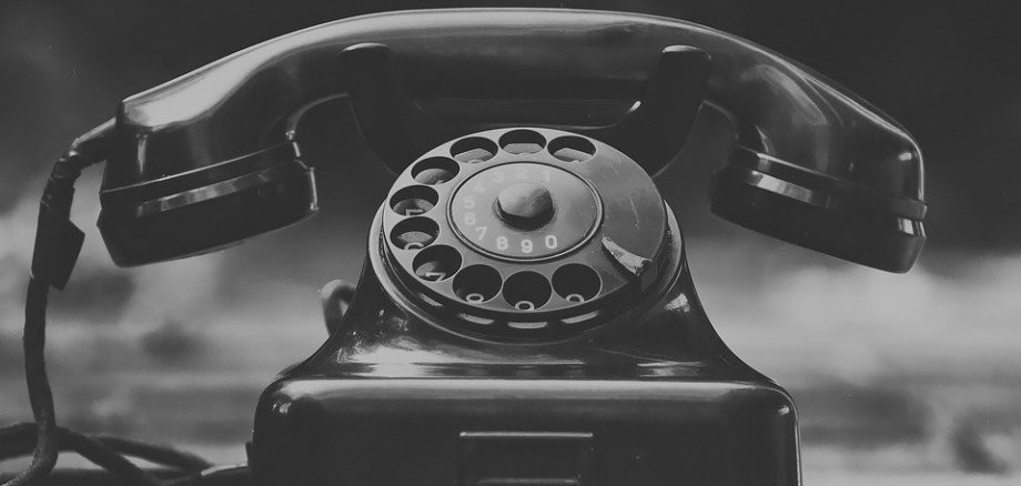 Auf dem Foto ist ein altes Telefon mit Wählscheibe zu sehen. Das Foto ist in schwarz-weiß dargestellt.