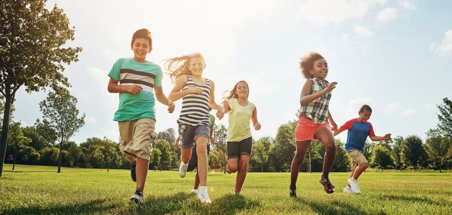 Happy friends, children and running with grass field in nature for fun, playful day or sunshine at park. Diversity or group of excited kids or youth enjoying sunny outdoor holiday or weekend together